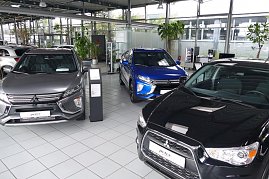 Innenansicht eines Autohauses mit mehreren Mitsubishi-Fahrzeugen in verschiedenen Farben, darunter ein grauer, ein blauer und ein schwarzer Wagen, auf glänzendem Fliesenboden mit großen Pflanzen und Glaswänden im Hintergrund. (Foto: Fischer/Autohaus Peter)