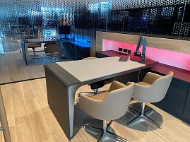 Modern eingerichtetes Verkäuferbüro im Autohaus mit hellem Holzboden, stilvollem Tisch, bequemen Stühlen und Computerarbeitsplatz. Im Hintergrund Glaswand mit Punktmuster. (Foto: Arenswald / Autohaus Peter)