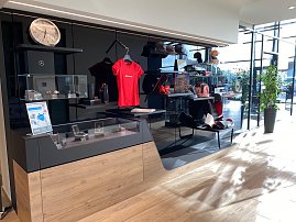 Mercedes-Benz Collection: Verkaufsbereich im Autohaus mit Verkaufsregalen, auf denen Mercedes-Fanartikel wie Shirts, Uhren und Mützen ausgestellt sind. Viel Tageslicht durch große Fenster. (Foto: Arenswald / Autohaus Peter)
