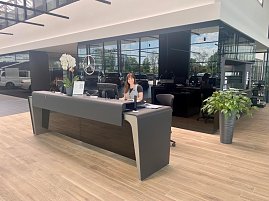Freundliche Mitarbeiterin am modernen Empfangstresen eines Mercedes-Autohauses mit Holzfußboden, Pflanzen und großem Mercedes-Stern im Hintergrund. (Foto: Krüger / Autohaus Peter)