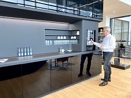 Mann im weißen Hemd zapft Kaffee am modernen Kaffeeautomaten in einer stilvollen Autohaus-Lounge mit Gläsern, Tassen und Wasserflaschen. (Foto: Krüger / Autohaus Peter)
