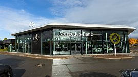 Modernes Mercedes-Benz Autohaus mit großer Glasfassade, Mercedes-Stern-Logo auf dem Dach und bepflanztem Mercedes-Symbol, blauer Himmel mit Wolken. (Foto: Steve Dornhofer/Autohaus Peter)