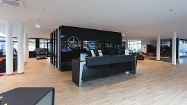 Moderner Empfangsbereich eines Mercedes-Benz Autohauses mit heller Holzoptik, schwarzem Empfangstresen, Glastrennwänden und Mercedes-Logo an der Wand. (Foto: Steve Dornhofer/Autohaus Peter)