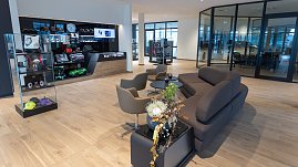 Moderner Wartebereich in einem Mercedes-Benz Autohaus mit bequemer grauer Couch, Sesseln, Glastischen, Blumenarrangement und Vitrine mit Mercedes-Accessoires und Fanartikeln. (Foto: Steve Dornhofer/Autohaus Peter )