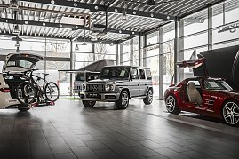 Innenraum einer modernen Mercedes-Benz-Ausstellungshalle mit großen Glasfronten. Zu sehen sind ein weißer Kombi mit offenem Kofferraum und Fahrradträger, ein silberner Mercedes G-Klasse SUV und ein roter Sportwagen mit geöffneten Flügeltüren. Heller, industrieller Boden und Decke mit Lampen. (Foto: Eric Freytag)