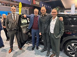Vier Männer (u.a. Mario Voigt und Andreas Peter) stehen lächelnd neben einem schwarzen Auto mit geöffneter Tür. Im Hintergrund sind die Logos von Opel, Volvo und Renault Trucks auf Bannern zu erkennen. (Foto: Autohaus Peter )