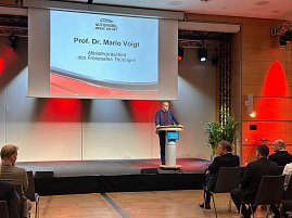 Prof. Dr. Mario Voigt spricht am Rednerpult der Messe Erfurt, im Hintergrund eine Leinwand mit seinem Namen und Titel als Ministerpräsident Thüringens. (Foto: Autohaus Peter )