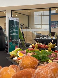 Nahaufnahme eines Buffets mit belegten Brötchen, Obst, Gemüse und Käseplatten. Daneben steht ein Begrüßungsaufsteller zum koda Unternehmerfrühstück. (Foto: Autohaus Peter)