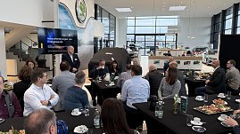 Torsten Wiesner hält einen Vortrag mit der Präsentation „Herausforderungen der Energiewende“. Teilnehmende sitzen an runden Tischen mit Kaffee und Frühstücksplatten. (Foto: Autohaus Peter)