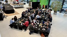 Blick von oben auf den Ausstellungsraum. Mehrere lange Tische sind mit Frühstück gedeckt. Viele Unternehmerinnen und Unternehmer sitzen und diskutieren. Links im Bild ein abgedecktes Fahrzeug. (Foto: Autohaus Peter)