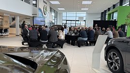 Rückansicht der Gäste, die an Frühstückstischen sitzen und einer Präsentation zuhören. Links im Bild die Rednerin, rechts der große koda-Schriftzug an der Wand. (Foto: Autohaus Peter)