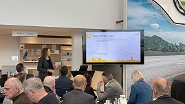 Eine Rednerin zeigt auf eine Folie mit Diagrammen und dem Titel „Herausforderungen“. Im Vordergrund sitzen Teilnehmende, die zuhören. (Foto: Autohaus Peter)
