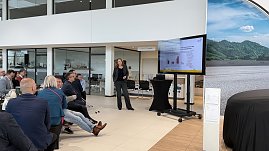 Teilnehmende verfolgen einen Vortrag im hellen koda-Ausstellungsraum. Ein Bildschirm zeigt Diagramme, im Vordergrund Frühstückstische. (Foto: Autohaus Peter)
