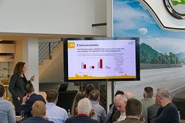 Teilnehmende verfolgen einen Vortrag im hellen koda-Ausstellungsraum. Ein Bildschirm zeigt Diagramme, im Vordergrund Frühstückstische. (Foto: Autohaus Peter)