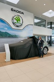 Ein koda Elroq ist noch mit einem schwarzen Tuch abgedeckt. Ein Mitarbeiter zieht die Abdeckung teilweise zur Seite. Das große koda-Logo hängt an der Wand. (Foto: Autohaus Peter)