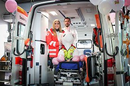Ein geöffneter Rettungswagen steht im Autohaus. Zwei Mitarbeitende des Deutschen Roten Kreuzes stehen darin, vor ihnen sitzt ein großes Stoff-Einhorn auf einer Krankentrage. Rosa Luftballons schmücken den Wagen. (Foto: Autohaus Peter)
