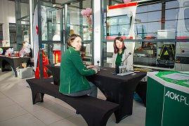 Zwei Frauen sitzen an einem schwarzen Tisch mit Infomaterial. Im Hintergrund steht ein Rettungswagen. Auf dem Tisch liegen Geräte, vermutlich für eine Mitmachaktion. Rechts ist ein grüner Stand der AOK Plus zu sehen. (Foto: Autohaus Peter)