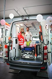 Ein geöffneter Rettungswagen steht im Autohaus. Zwei Mitarbeitende des Deutschen Roten Kreuzes stehen darin, vor ihnen sitzt ein großes Stoff-Einhorn auf einer Krankentrage. Rosa Luftballons schmücken den Wagen. (Foto: Autohaus Peter)
