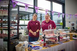 Zwei Frauen stehen hinter einem Kuchen- und Tortenstand im Autohaus. In einer Glasvitrine und auf Tischen sind Cupcakes und Torten ausgestellt. Rosa Flamingos dienen als Dekoration. Ein Banner mit dem Logo „Happy Cakes“ hängt über dem Stand. (Foto: Autohaus Peter)