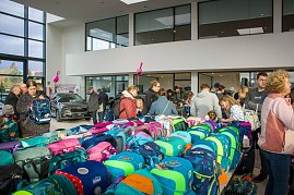 Viele Besucher stehen an Tischen voller bunter Schulranzen. Im Hintergrund ist ein schwarzes koda-Fahrzeug ausgestellt, rosa Flamingos hängen von der Decke. (Foto: Autohaus Peter)