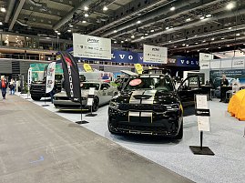 Ein schwarzer Dodge mit gelben Rallyestreifen vorne und ein grauer Dodge Challenger stehen nebeneinander. Daneben schwarze RAM-Fahrzeuge mit großen Bannern. (Foto: Autohaus Peter Gruppe)