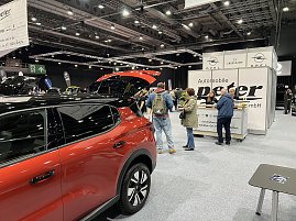Besucher stehen vor dem Info-Counter von Autohaus Peter. Daneben ein rotes Opel-Fahrzeug mit geöffnetem Kofferraum. (Foto: Autohaus Peter Gruppe)