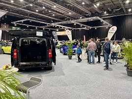 Schwarzer Transporter mit geöffneter Heckklappe, ausgestellt auf der Messe. Besucher laufen durch die Halle, viele Fahrzeuge im Hintergrund. (Foto: Autohaus Peter Gruppe)