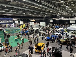 Breiter Überblick über die Automobilmesse mit dichten Besuchergruppen, Fahrzeugen aller Marken und farbigen Ausstellungsflächen. (Foto: Autohaus Peter Gruppe)