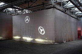 Großes, verhülltes Objekt mit Mercedes-Stern-Projektionen in einer Halle vor einer Enthüllung. (Foto: Daimler Truck AG)