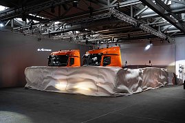 Zwei orangefarbene Mercedes-Benz eActros-Lkw mit Schade-Logo, teilweise noch von einer weißen Abdeckung umhüllt. (Foto: Daimler Truck AG)