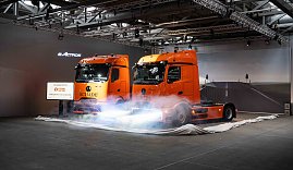 "Zwei orangefarbene Mercedes-Benz eActros-Lkw mit Schade-Logo während einer Fahrzeug-Enthüllung mit Nebeleffekten. (Foto: Daimler Truck AG)