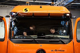 Zwei Männer prüfen das Fahrerhaus eines orangefarbenen Mercedes-Benz eActros von innen. (Foto: Daimler Truck AG)