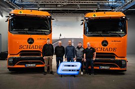 Das Team von Schade Logistic posiert mit 5 Personen vor zwei orangefarbenen Mercedes-Benz eActros-Lkw mit Schade-Logo und leuchtendem E-Symbol. (Foto: Daimler Truck AG)
