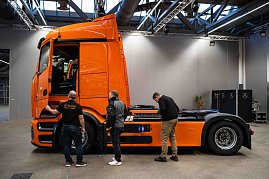 Drei Männer betrachten die Seite eines orangefarbenen Mercedes-Benz eActros in einer Halle. (Foto: Daimler Truck AG)