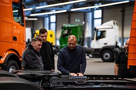 Mehrere Männer inspizieren technische Details am Fahrgestell eines orangefarbenen Mercedes-Benz eActros in einer Produktionshalle. (Foto: Daimler Truck AG)