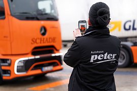 Frau im schwarzen Autohaus Peter-Jacke fotografiert einen orangefarbenen Mercedes-Benz eActros mit dem Handy. (Foto: ex animo MEDIA)