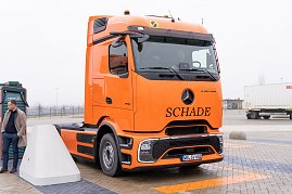 "Orangefarbener Mercedes-Benz eActros mit Schade-Logo auf einem Parkplatz, daneben eine Person und eine Ladesäule. (Foto: ex animo MEDIA)