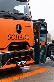 Detailaufnahme eines orangefarbenen Mercedes-Benz eActros mit Schade-Logo an einer grünen Schnellladesäule mit 400 kW. (Foto: ex animo MEDIA)