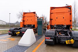 Heckansicht von zwei eActros 600 Lkw beim Laden. Zwischen den Fahrzeugen steht eine große Ladesäule, im Hintergrund mehrere Personen. (Foto: ex animo MEDIA)