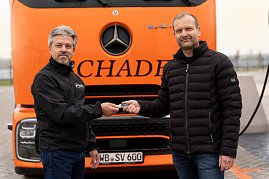 Schlüsselübergabe: Frank Hentschel, Verkaufsleiter Trucks bei Autohaus Peter GmbH, übergibt symbolisch den Fahrzeugschlüssel an Björn Schade, Geschäftsführer Schade Logistics. Beide stehen vor einem orangefarbenen eActros. (Foto: ex animo MEDIA)