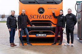 Vier Personen vor einem orangefarbenen Mercedes-Benz eActros-Lkw mit Schade-Logo. Eine Person zeigt auf das eActros-Emblem. Abgebildet von links nach rechts: Frank Hentschel (Verkaufsleiter Trucks, Autohaus Peter GmbH), Björn Schade (Geschäftsführer Schade Logistics), Christina Dost (Geschäftsführerin Autohaus Peter GmbH), Enrico Dost (Serviceleiter). (Foto: ex animo MEDIA)