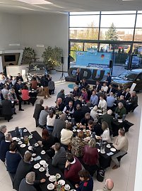 Blick von oben auf viele Vertreter der Wirtschaft, die an schwarzen Tischen mit Kaffee und Gebäck sitzen. Vorne steht ein Redner, hinten ist eine Bühne mit CDU-Logo und Bannern zu sehen. (Foto: Autohaus Peter)
