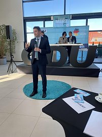 David Gregosz im Anzug spricht vor Publikum in einer Autohaus-Halle. Hinter ihm Bühne mit CDU-Logo und Podiumsteilnehmern, vorne auf dem Tisch Broschüren und eine Tasse. (Foto: Autohaus Peter)