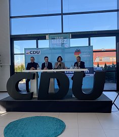 Frontalaufnahme der Podiumsdiskussion mit vier Personen, mittig Colette Boos-John. Vor ihnen große CDU-Buchstaben, im Hintergrund „Team Merz 2025“-Plakat. (Foto: Autohaus Peter)