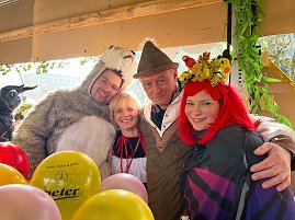"Vier Personen in farbenfrohen Kostümen  darunter ein Bärenkostüm, ein Dirndl und ein Fantasiekostüm mit roter Perücke  stehen beieinander und lächeln in die Kamera, umgeben von bunten Luftballons. (Foto: Autohaus Peter GmbH)