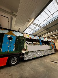 Seitliche Ansicht eines bunt bemalten Karnevalswagens in einer Halle, verziert mit Burgmotiven, Blumen und Wolken. (Foto: Autohaus Peter GmbH)