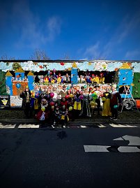 Große Gruppe verkleideter Menschen posiert vor und auf einem bunt gestalteten Karnevalswagen mit Märchenmotiven, viele halten bunte Luftballons. (Foto: Autohaus Peter GmbH)