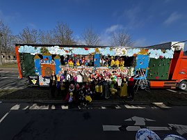 Große Gruppe verkleideter Menschen posiert vor und auf einem bunt gestalteten Karnevalswagen mit Märchenmotiven, viele halten bunte Luftballons. (Foto: Autohaus Peter GmbH)