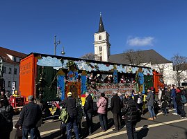 Karnevalswagen mit Burg- und Wolkenmotiven fährt durch eine Innenstadt, Menschen stehen am Straßenrand und schauen zu, im Hintergrund eine Kirche mit Turm. (Foto: Autohaus Peter GmbH)