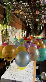 "Reihe bunter Luftballons mit der Aufschrift Helau, Alaaf & Ahoi! und dem Autohaus-Peter-Logo, befestigt an weißen Stäben, unter einer mit Pflanzen und Sternen dekorierten Decke. (Foto: Autohaus Peter GmbH)